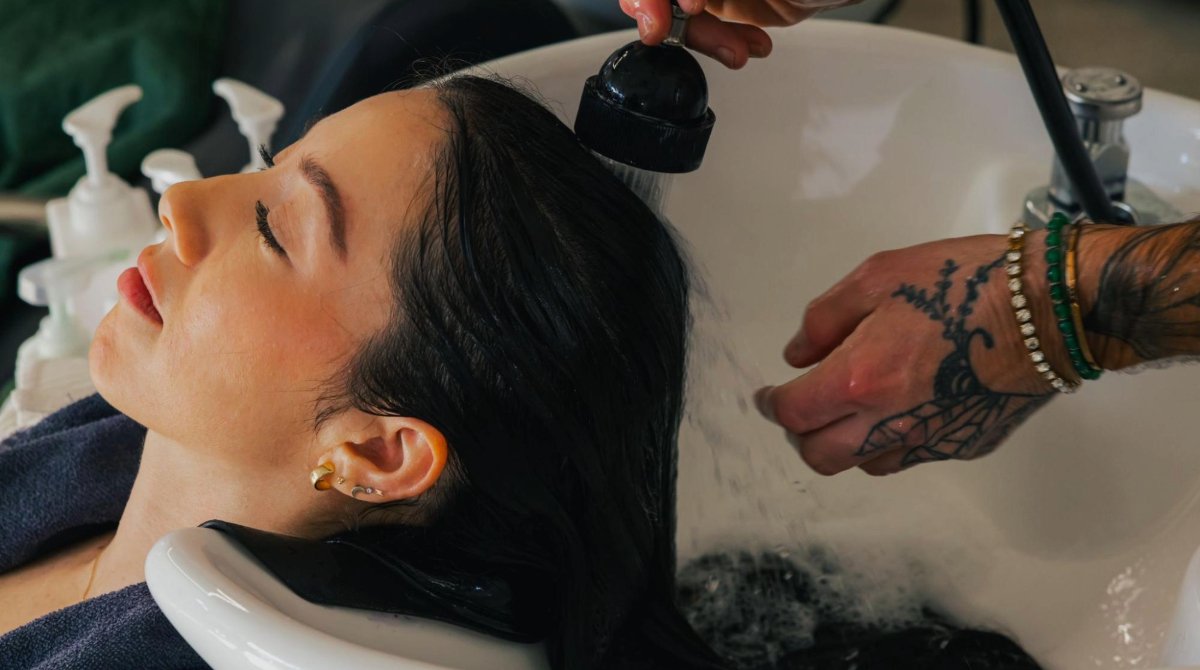 A salon client with long, dark hair leans back for a hair wash.