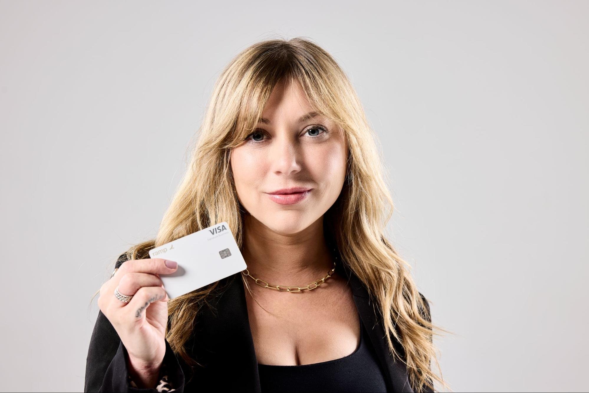 A woman shows a slight smile as she holds up a Visa card.
