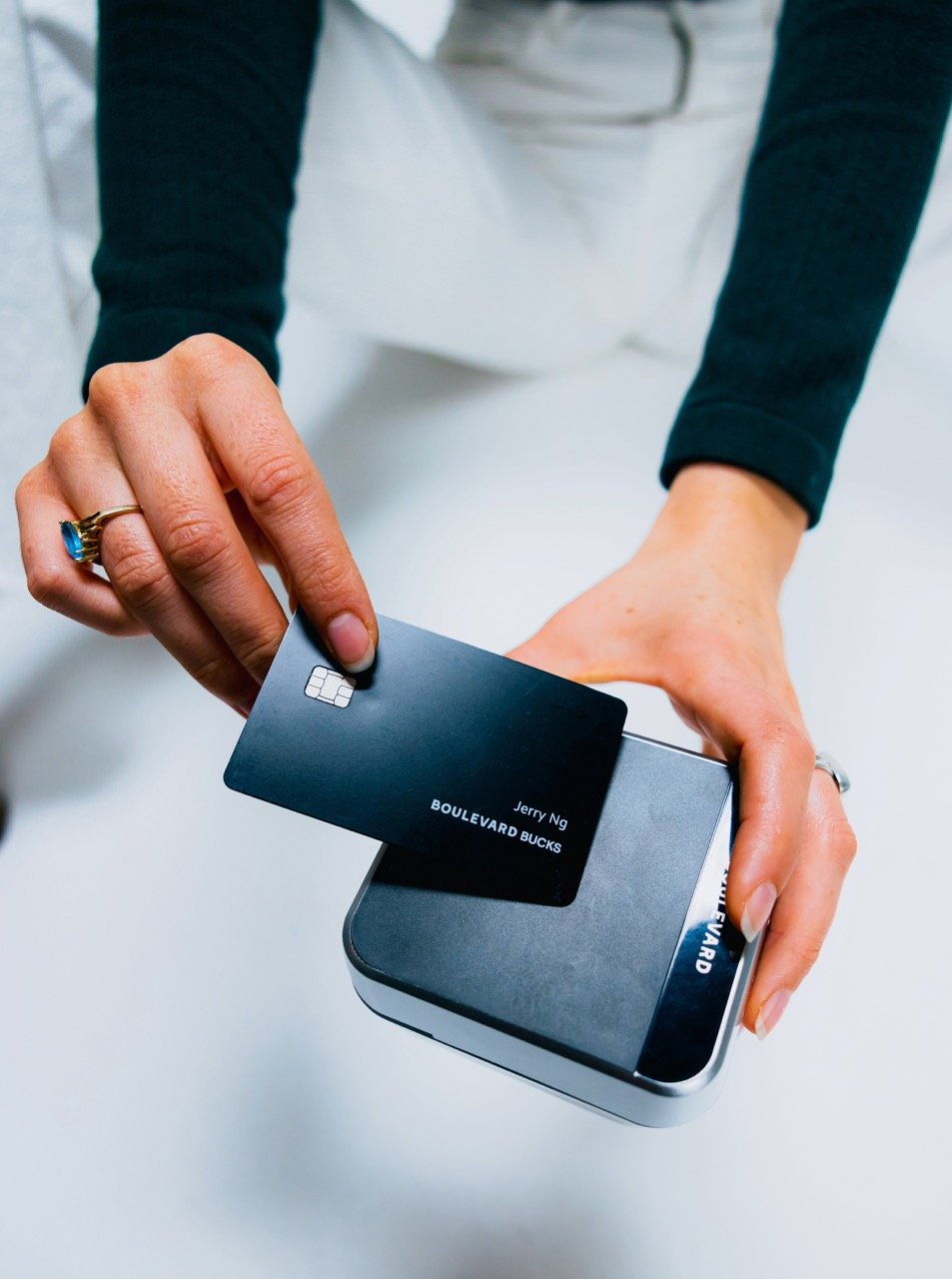 Arm are shown extended with their hands at the center of the photo, with one holding a credit card to a payment device that is held in the other hand.