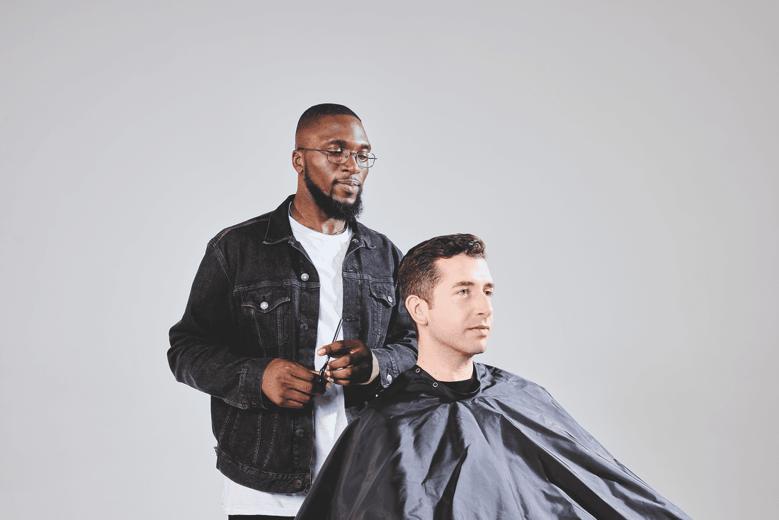 A barber tending to a client in a chair covered in a black smock. 