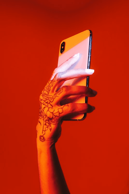 A tattooed hand holds up a smartphone against a crimson background.