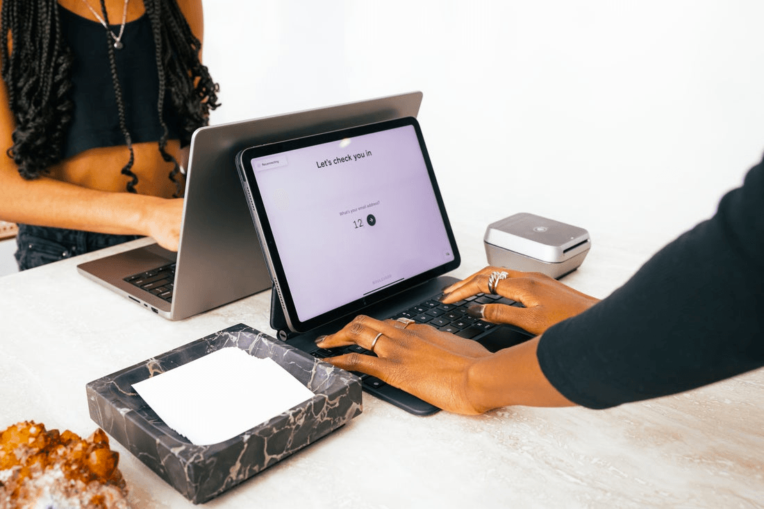 A pair of hands rests atop a keyboard that is connected to a tablet. The words "Let's check you in" are on the screen.